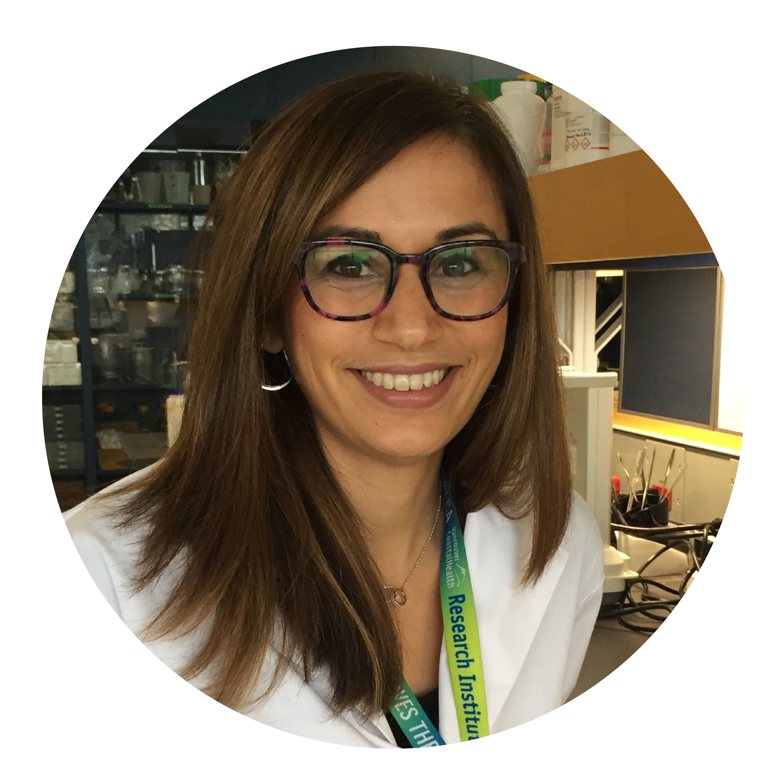 A woman in a white coat, green lanyard and brown glasses with medium lenght brown hair