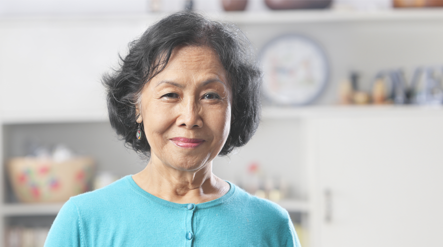 Older woman in bright sweater stands in kitchen