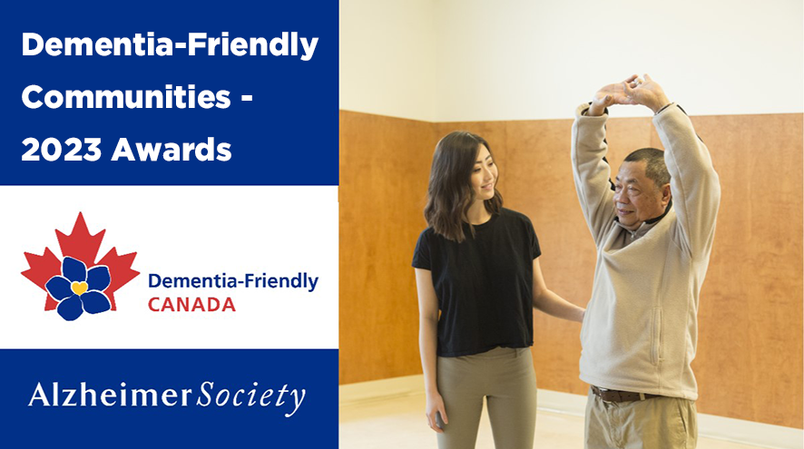 Mario, who lives with dementia, practices a stretching exercise while a friendly instructor helps. The text "Dementia-Friendly Communities - 2023 Awards" can be read to the left of Mario and the instructor.