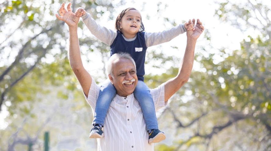 Older man in short button down shirt carries young child on shoulders