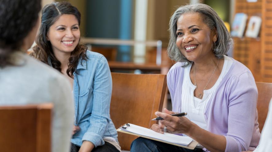 woman smiling and taking notes while meeting with colleagues