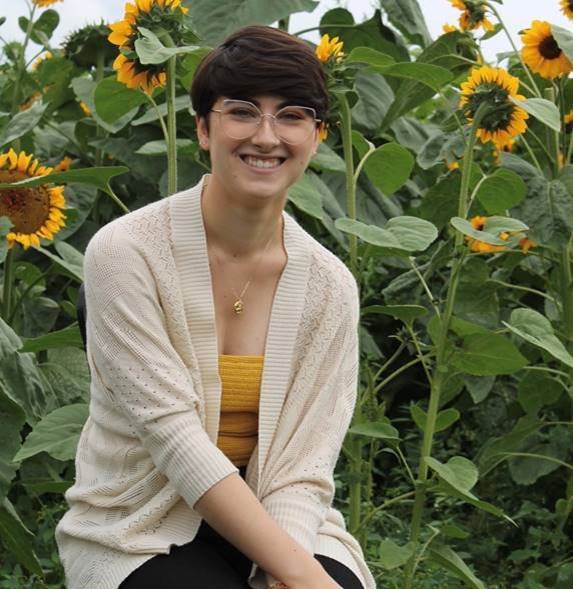 Bridget smiling in front of a field of sunflowers.