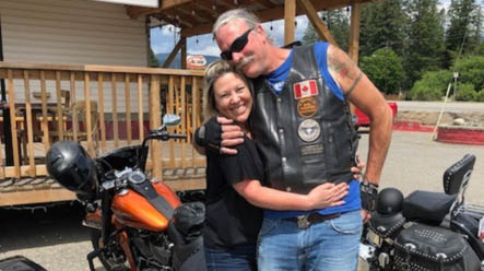 Man and woman happily embrace outside beside a orange motorcycle 