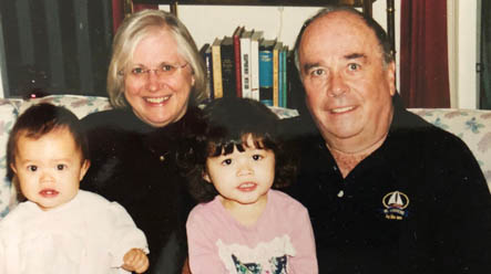 A happy grandma and grandpa sit on a couch with their two happy baby grandchildren