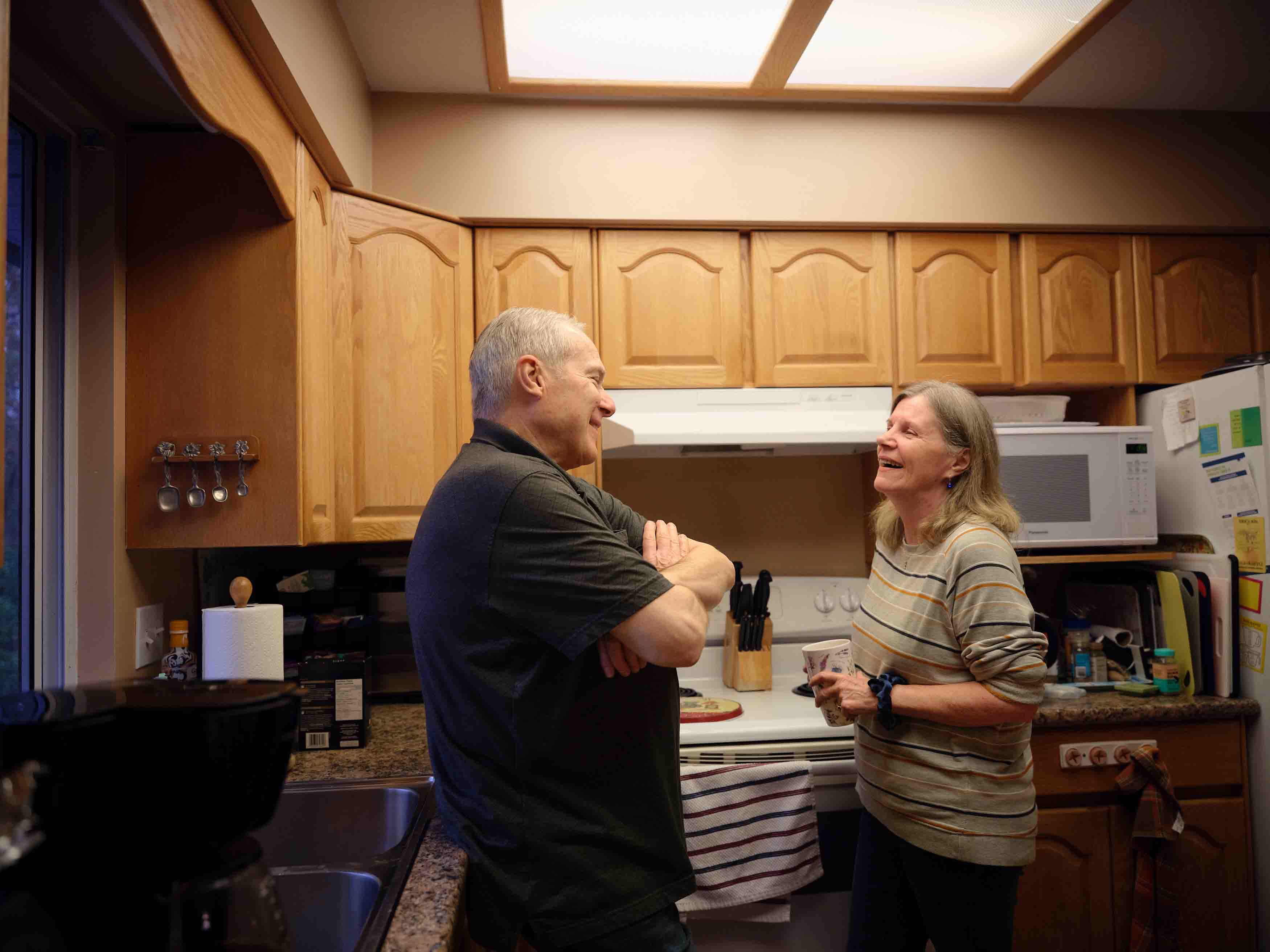 An older man and a woman smiling and talking together in a kitchen.