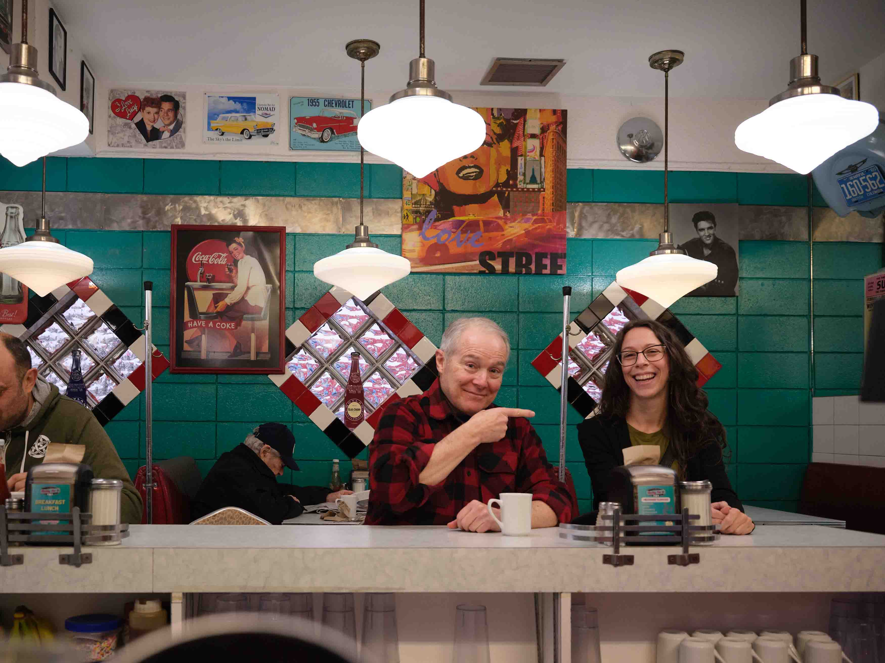 An older man and a woman smiling together at the counter of a colourful diner.