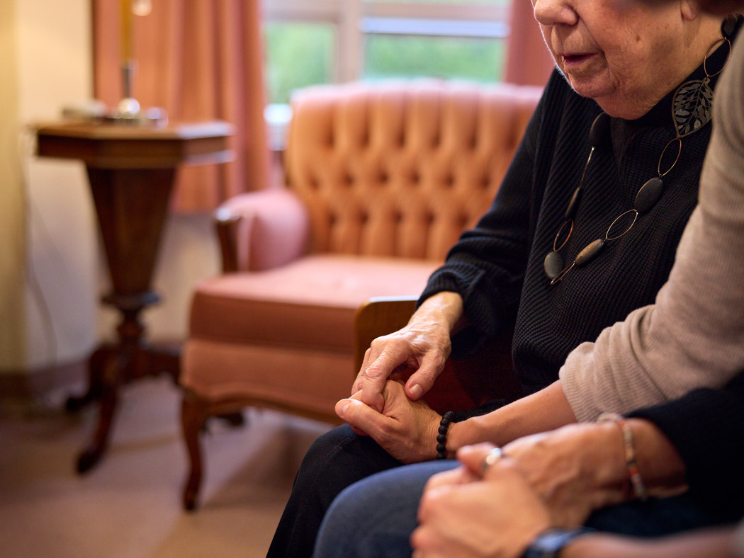 An older woman holding hands with another person while they sit together.