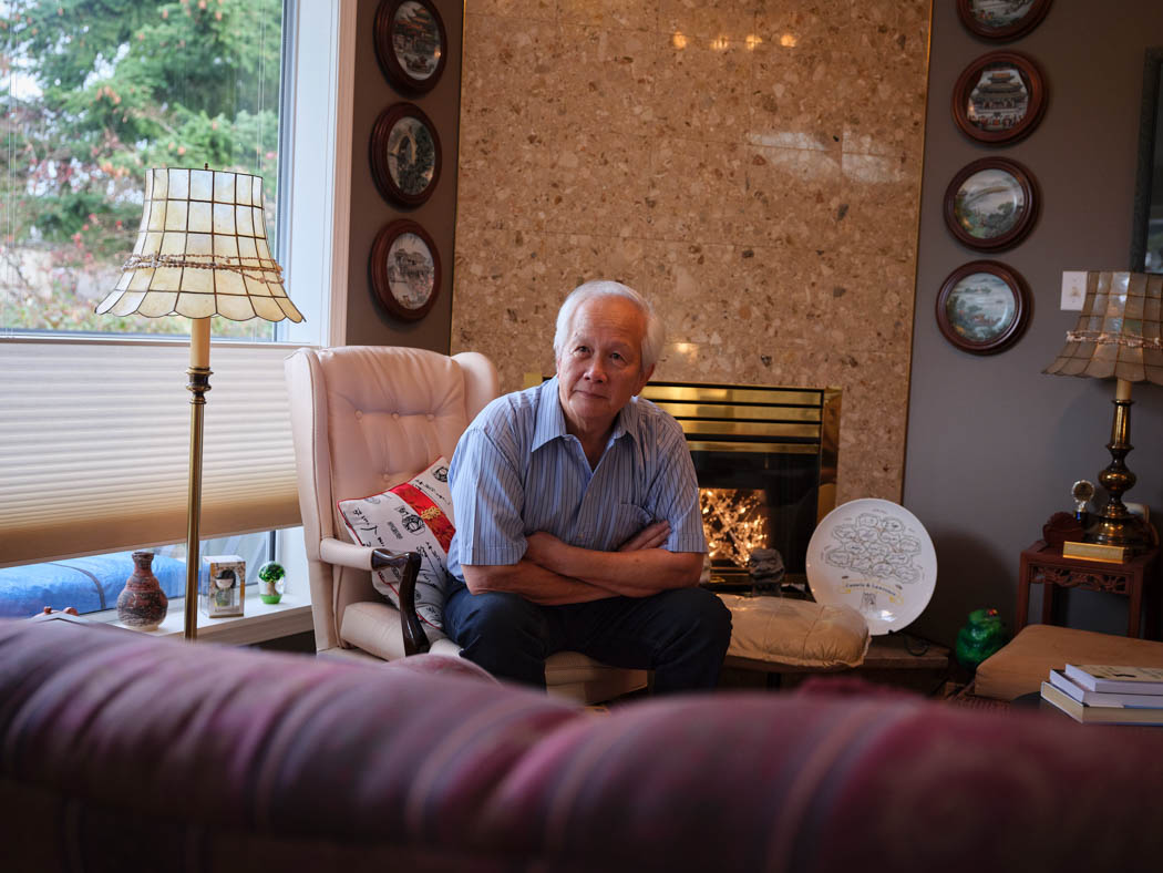 An older man sits in an armchair in a warmly decorated living room.