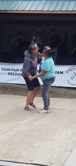 Two people embrace while dancing together outdoors in front of a stage.