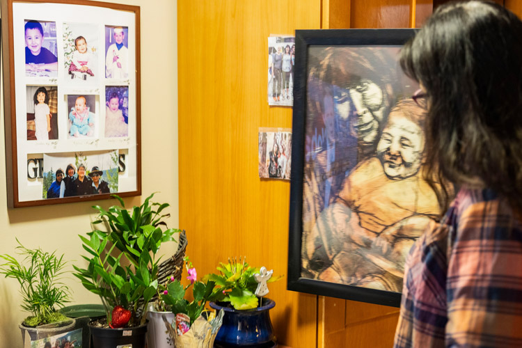 A woman looks at a framed portrait displayed among flowers and photographs.