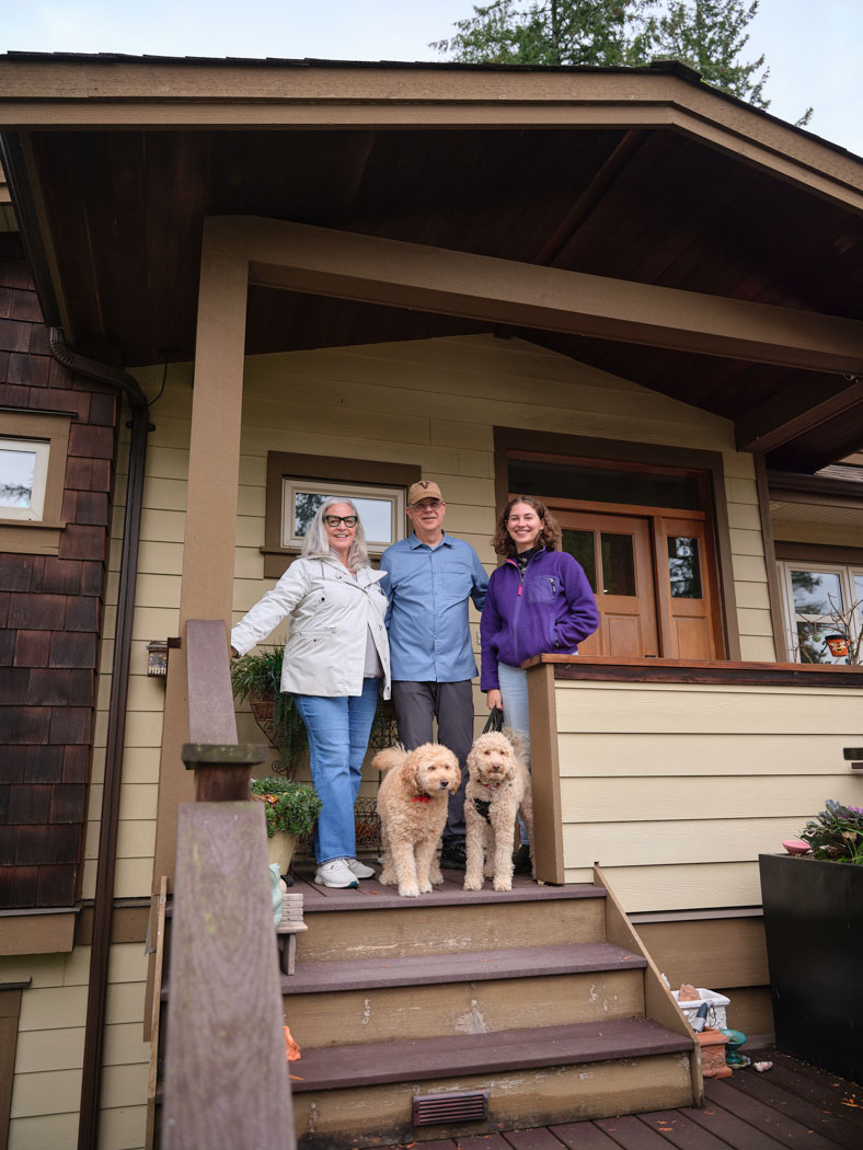 Three people stand with a dog on the front steps of a house, smiling for the camera.