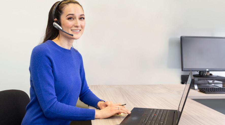 Helpline volunteer dressed in blue at the laptop, smiling at the screen.