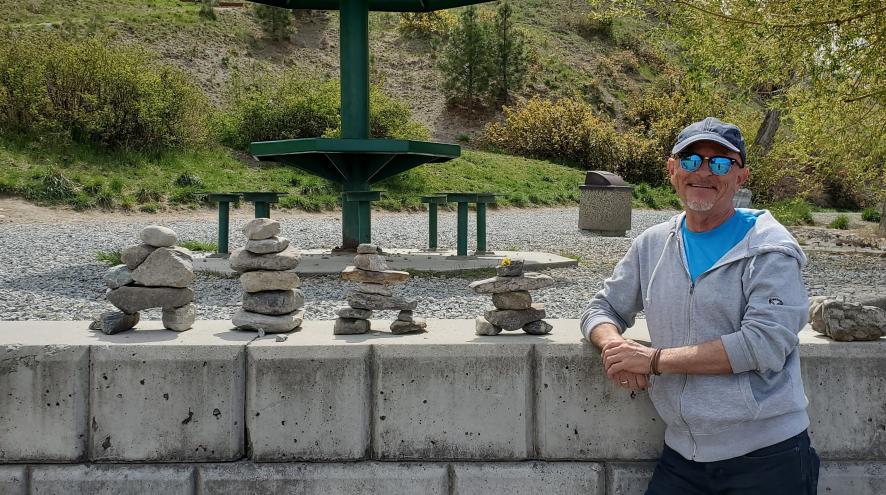 Craig wearing sunglasses and a hat, standing in front of a wall with stone stacking.