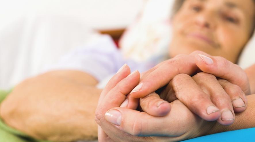 An elderly woman smiling and holding another person's hand.