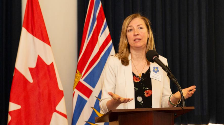 Maria speaking in front of the Canadian and British Columbian flag.