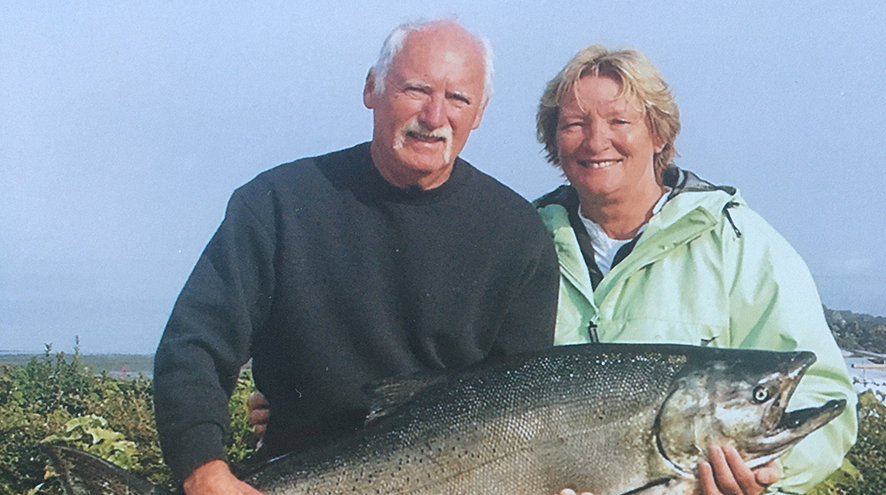 An older white man with white hair smiles next to a white woman with a short, blond bob. They are holding a massive fish.