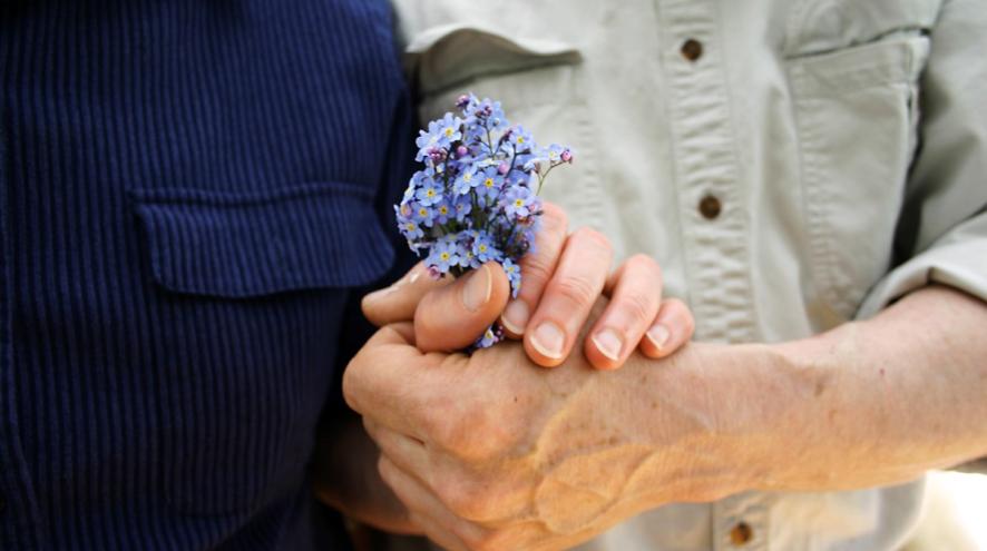 Two people holding hands, with a bundle of forget-me-not flowers.