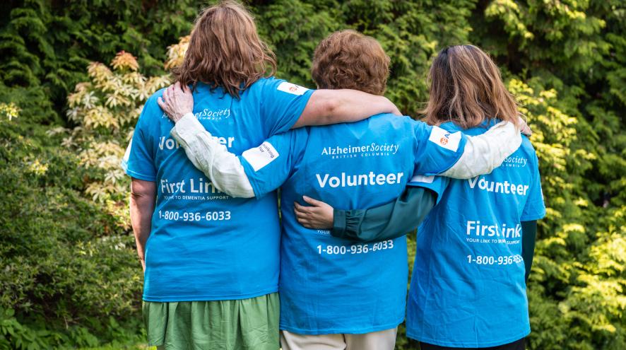 Three people wearing volunteer t-shirts with their arms around one another's shoulders