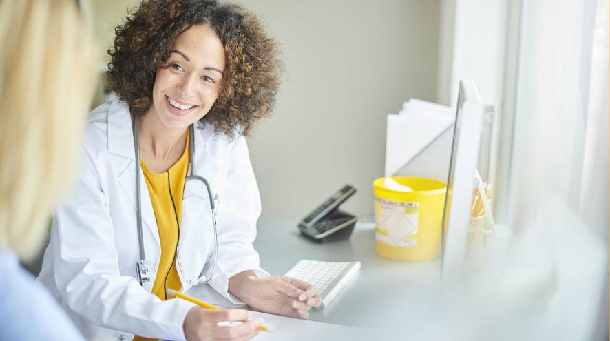 A  friendly young doctor, wearing a yellow shirt and white lab coat, speaks to a patient we can't see