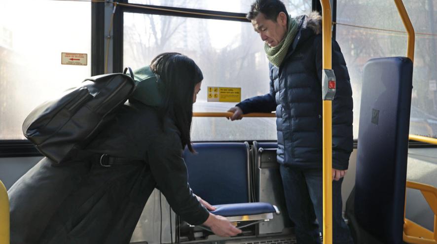 A woman helps a man with his seat on a public bus