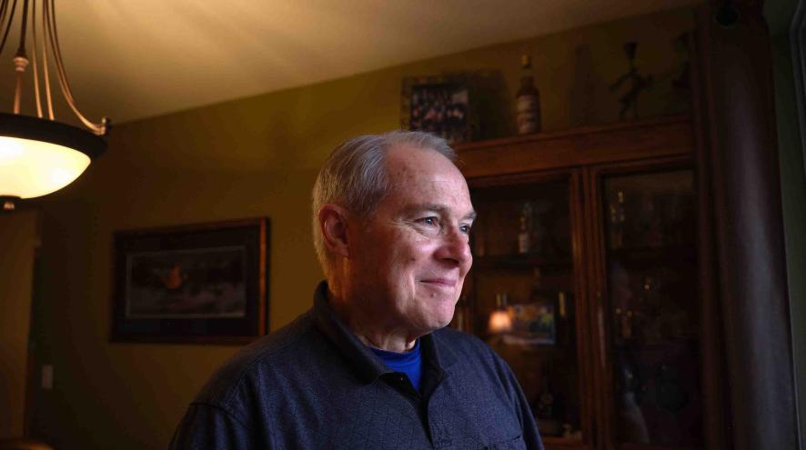 Older man smiling while standing in a warmly lit room.
