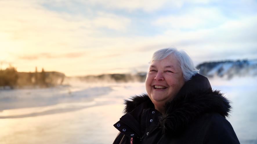 Photo of Pat Hanrath, smiling outdoors and standing on a snowy field. She is wearing a thick black winter coat.