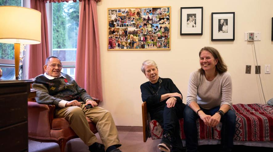 Three people sit together in a warmly decorated room, smiling and talking.