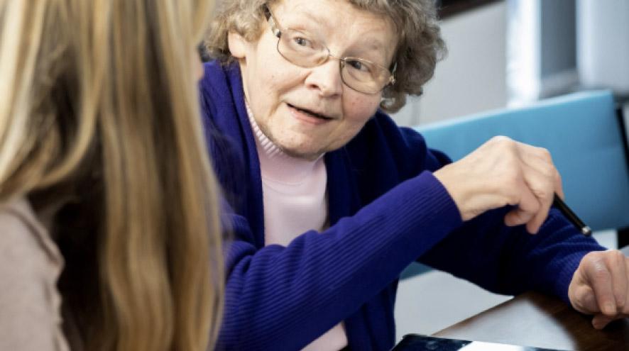 An elderly woman organizes her medication as a female nurse watches.