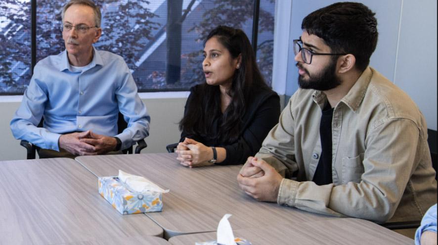 Three adults sitting at a table listening to a presentation