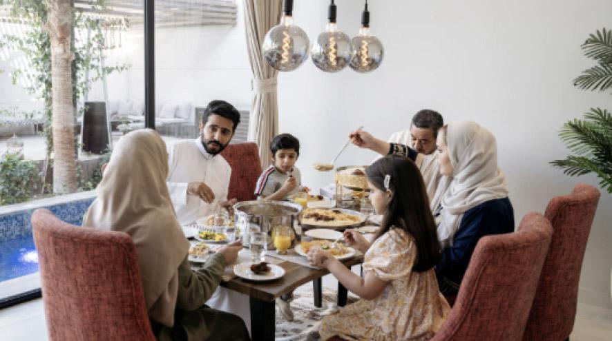 A family of all ages sits around a table, enjoying a meal together.