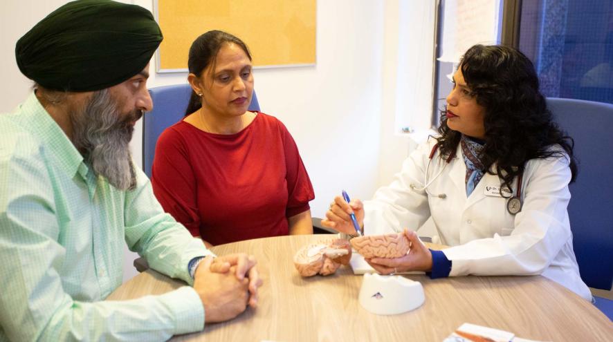 Two people meet with a doctor, who refers to a model of the brain.