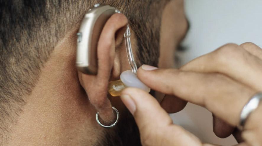 A man, wearing a silver earring and a ring on his finger, puts in and adjusts a hearing aid.