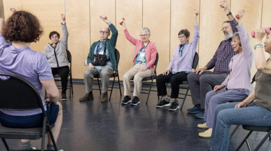 A group of diverse people sit in a circle, stretching on chairs.