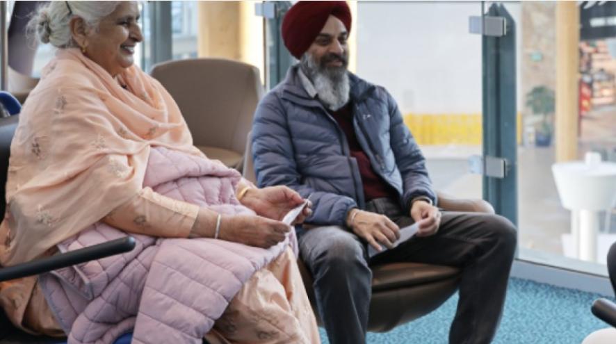 A woman and a man sit next to each other in the waiting room at an airport. They look happy.
