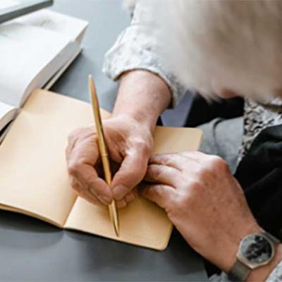 an elderly woman with her had down, writing in a journal