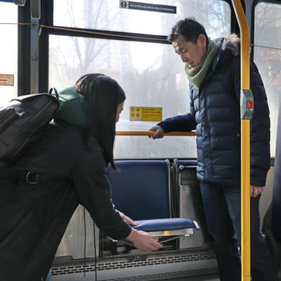 A woman helps a man with his seat on a public bus