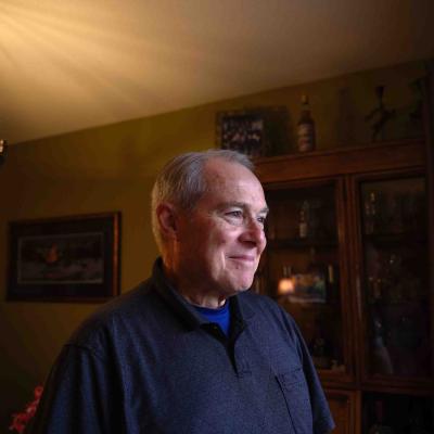 Older man smiling while standing in a warmly lit room.