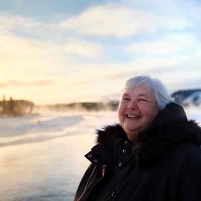 Photo of Pat Hanrath, smiling outdoors and standing on a snowy field. She is wearing a thick black winter coat.