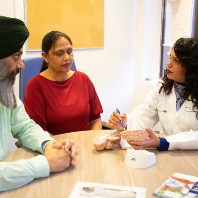 Two people meet with a doctor, who refers to a model of the brain.