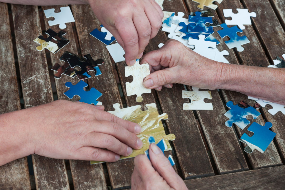 Two people doing a puzzle on a wooden surface.
