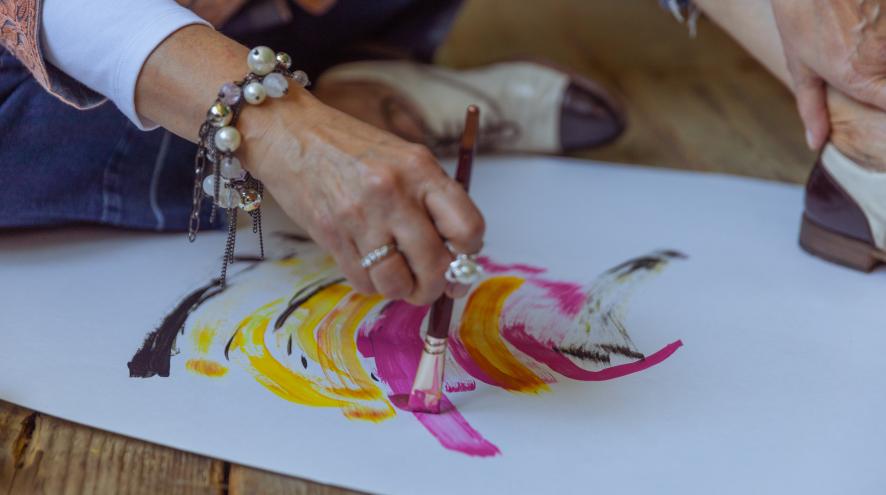 Woman's hand holding a paint brush with strokes of colour on paper.