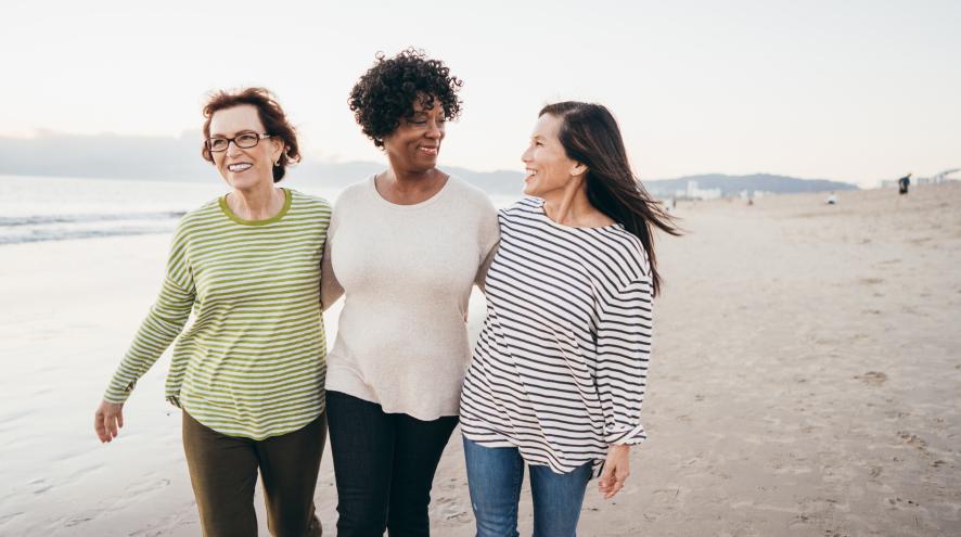 Three women walking arm in arm along a white sandy beach.