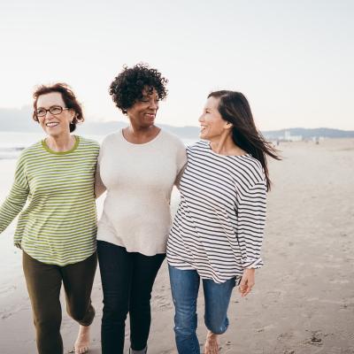 Three women walking arm in arm along a white sandy beach.