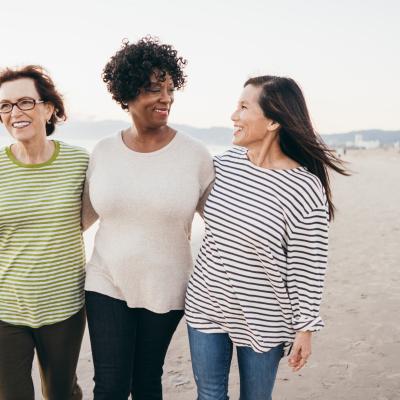 Three women walking arm in arm along a white sandy beach.