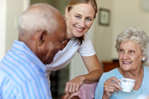 Young professional caregiver checking in with two happy seniors having tea.