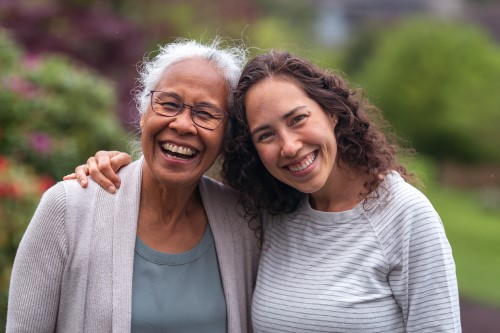 A smiling senior woman with her daughter, who is hugging her.