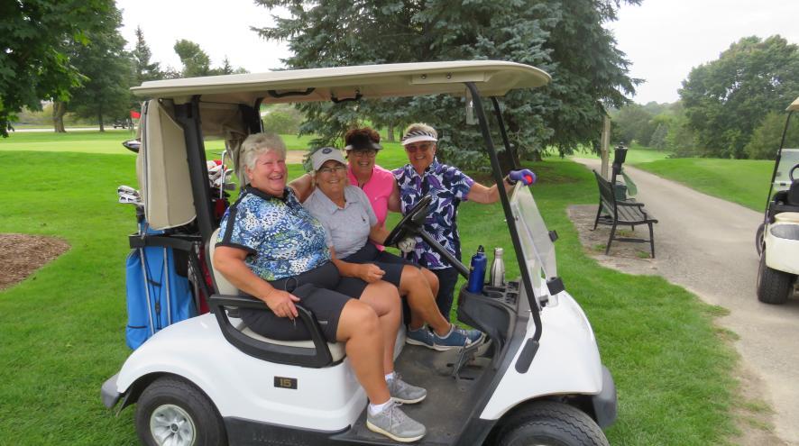Four people on a golf cart looking at the camera
