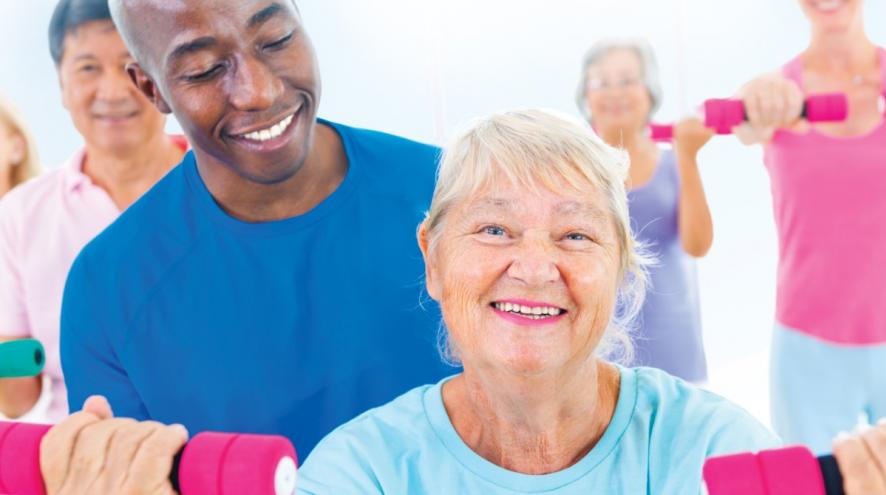 Man looking over a senior woman holding dumbbells.