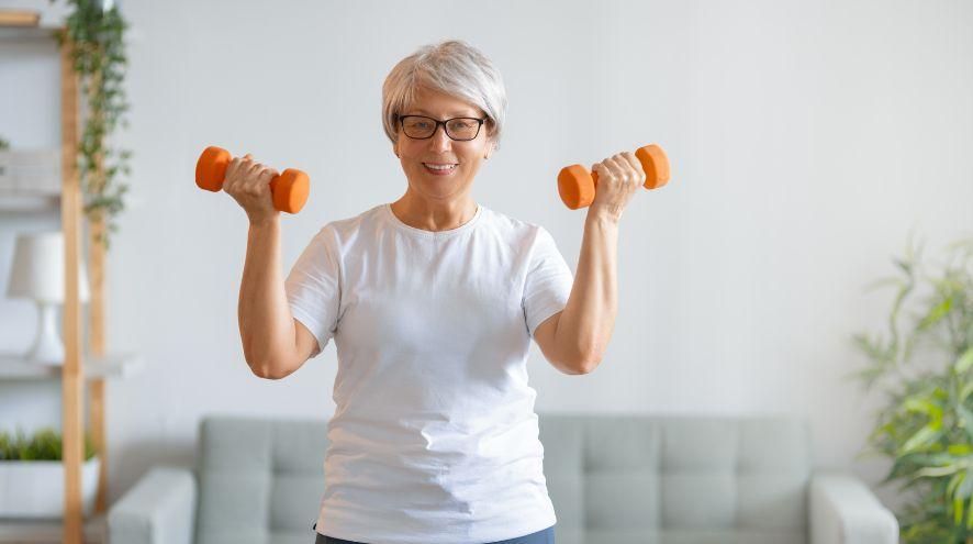A woman smiling and holding two small dumbbells