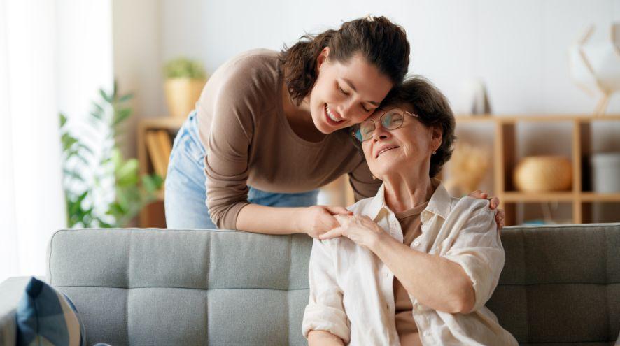 A woman holding an older woman's shoulder with a smile